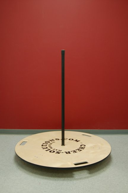 The Mat Mover II, a birch plywood disc and steel pole that a rolled cheer mat stands on